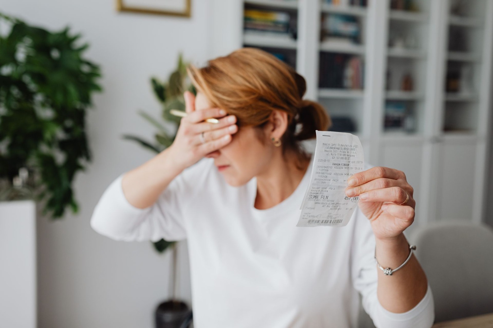 A stressed woman holding a receipt while covering her face with her hand