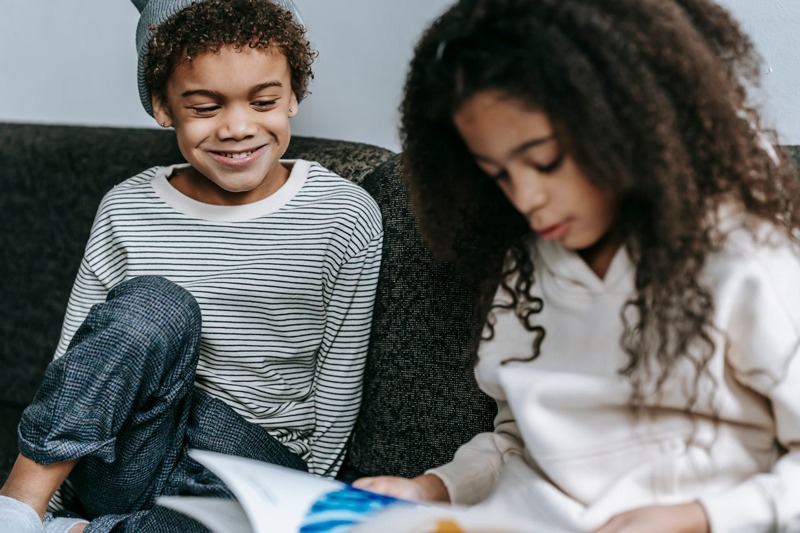 Two siblings reading a book together on a couch