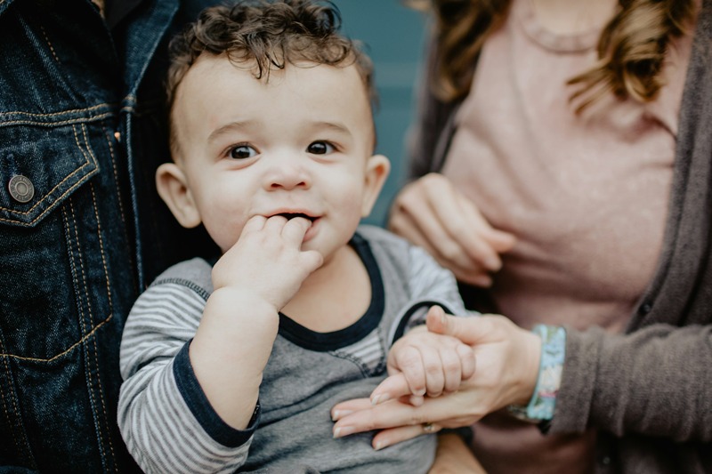 A toddler held between both parents, one hand held by each