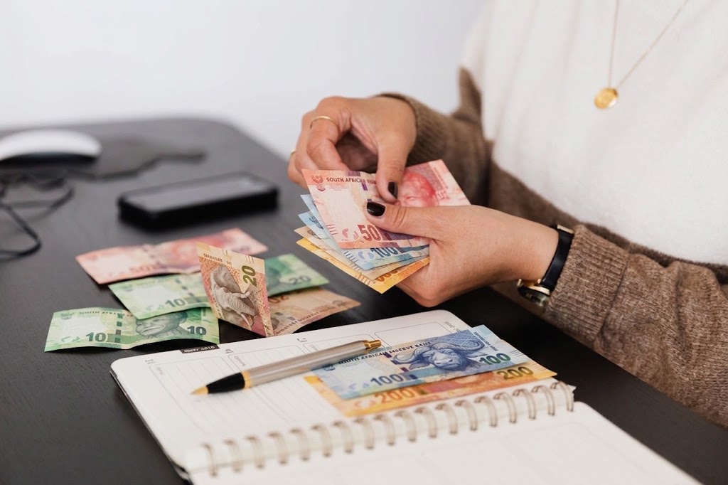 A woman counting South African rand notes at a desk while reviewing a planner